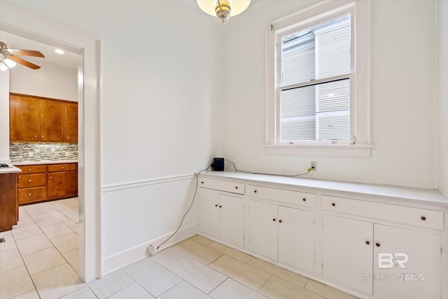 interior space with tile patterned floors, a wealth of natural light, a ceiling fan, and backsplash