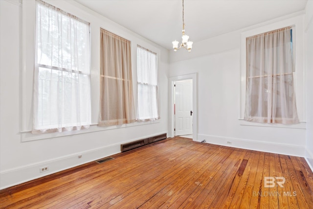 empty room with visible vents, hardwood / wood-style flooring, baseboards, and a notable chandelier