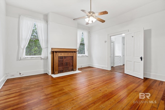 unfurnished living room with baseboards, hardwood / wood-style floors, a ceiling fan, and a healthy amount of sunlight