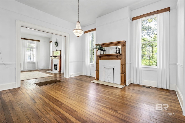unfurnished living room with wood-type flooring, an inviting chandelier, a fireplace with flush hearth, and visible vents