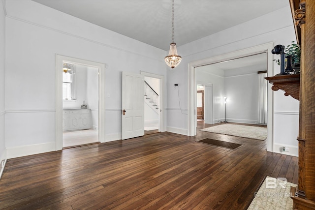 unfurnished dining area with stairway, an inviting chandelier, baseboards, and hardwood / wood-style floors