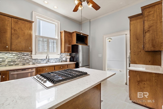 kitchen featuring a ceiling fan, brown cabinetry, a sink, tasteful backsplash, and appliances with stainless steel finishes