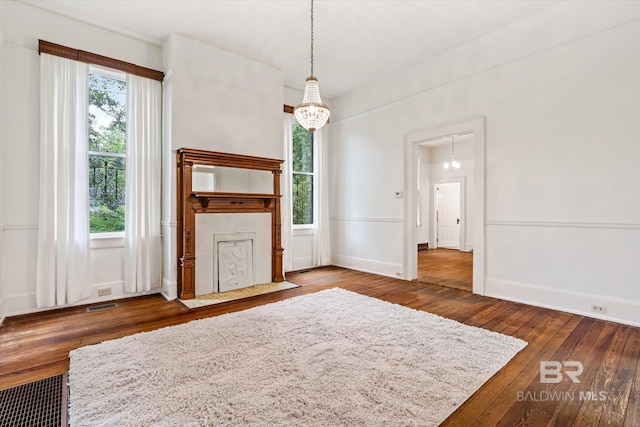 unfurnished living room with wood-type flooring, a notable chandelier, baseboards, and visible vents