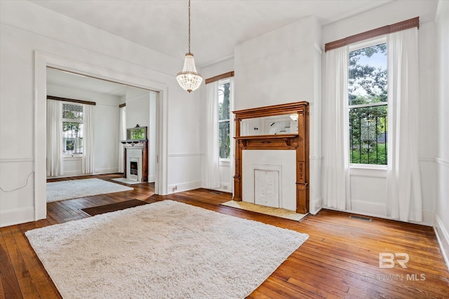 interior space featuring visible vents, a chandelier, wood-type flooring, baseboards, and a fireplace with flush hearth