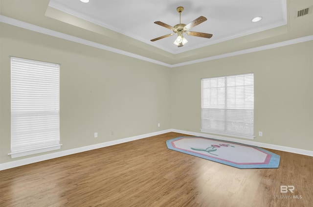 unfurnished room featuring a raised ceiling, ceiling fan, hardwood / wood-style floors, and crown molding