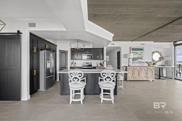 kitchen featuring a barn door, a kitchen island with sink, appliances with stainless steel finishes, and tasteful backsplash