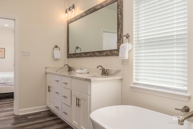 bathroom with a soaking tub, double vanity, a sink, and wood finished floors