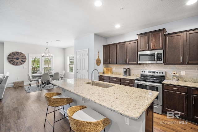 kitchen featuring dark brown cabinetry, a kitchen breakfast bar, light stone counters, a sink, and appliances with stainless steel finishes