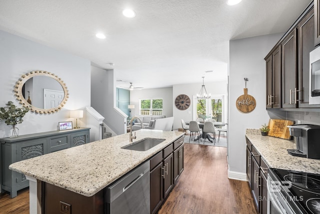 kitchen with stainless steel dishwasher, dark brown cabinetry, light stone countertops, an island with sink, and a sink