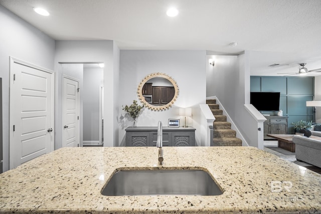 kitchen with a sink, light stone counters, a ceiling fan, and open floor plan