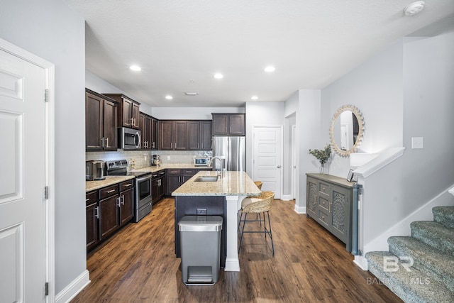 kitchen with dark brown cabinetry, a breakfast bar area, a sink, stainless steel appliances, and dark wood-type flooring