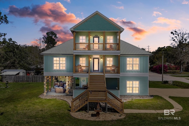 back house at dusk with a lawn, covered porch, and a balcony