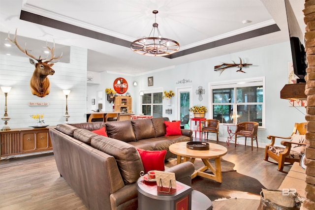 living room with a notable chandelier, wooden walls, ornamental molding, a raised ceiling, and light hardwood / wood-style flooring