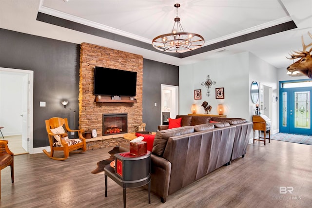 living room with ornamental molding, an inviting chandelier, a tray ceiling, a fireplace, and wood-type flooring