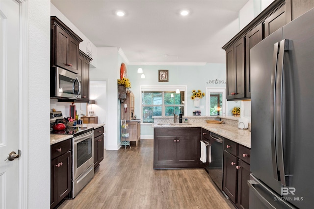 kitchen with dark brown cabinetry, kitchen peninsula, appliances with stainless steel finishes, ornamental molding, and light wood-type flooring