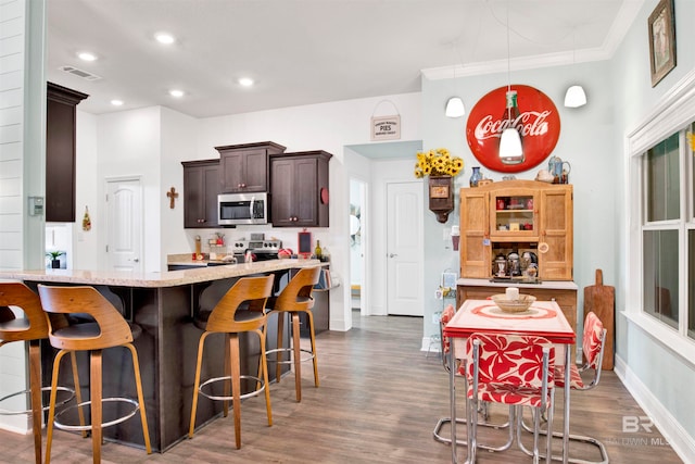 kitchen with dark brown cabinetry, a breakfast bar area, dark hardwood / wood-style floors, crown molding, and appliances with stainless steel finishes