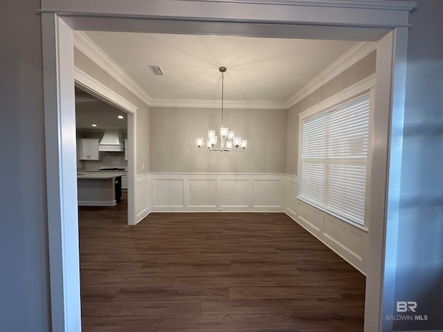 unfurnished dining area featuring dark wood-type flooring, crown molding, and a notable chandelier