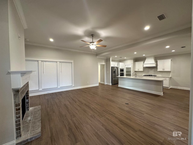 unfurnished living room featuring sink, ceiling fan, dark hardwood / wood-style floors, crown molding, and a brick fireplace