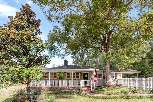 ranch-style house featuring covered porch, fence, a chimney, and ceiling fan