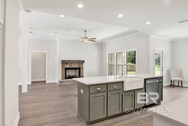 kitchen with stainless steel dishwasher, sink, a center island with sink, light hardwood / wood-style flooring, and a fireplace