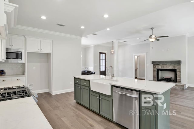 kitchen with a stone fireplace, sink, light hardwood / wood-style flooring, light stone countertops, and stainless steel appliances