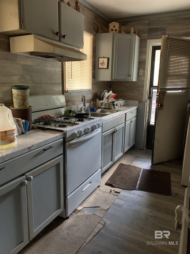 kitchen featuring gray cabinetry, wooden walls, white gas range oven, and a healthy amount of sunlight