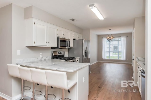 kitchen featuring a breakfast bar, white cabinets, appliances with stainless steel finishes, kitchen peninsula, and a chandelier