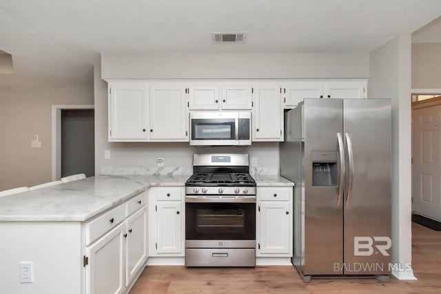 kitchen with white cabinets, a textured ceiling, appliances with stainless steel finishes, light hardwood / wood-style floors, and kitchen peninsula