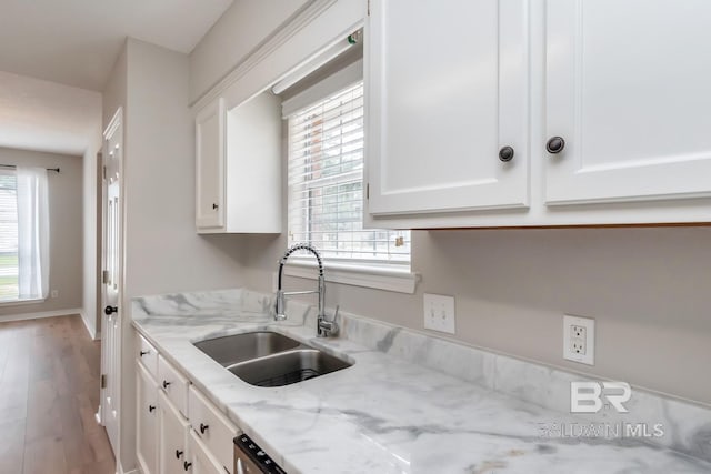 kitchen featuring light stone counters, a sink, white cabinetry, wood finished floors, and baseboards