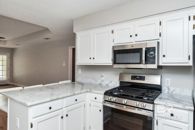 kitchen with kitchen peninsula, stainless steel appliances, white cabinets, and light stone counters