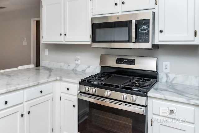 kitchen featuring white cabinetry, light stone countertops, appliances with stainless steel finishes, and a peninsula