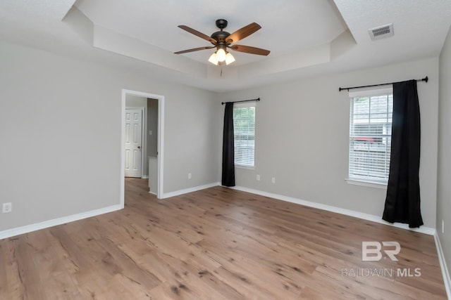 spare room with a raised ceiling, ceiling fan, and light wood-type flooring