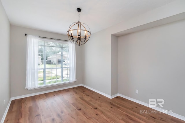 spare room with baseboards, wood finished floors, and a notable chandelier