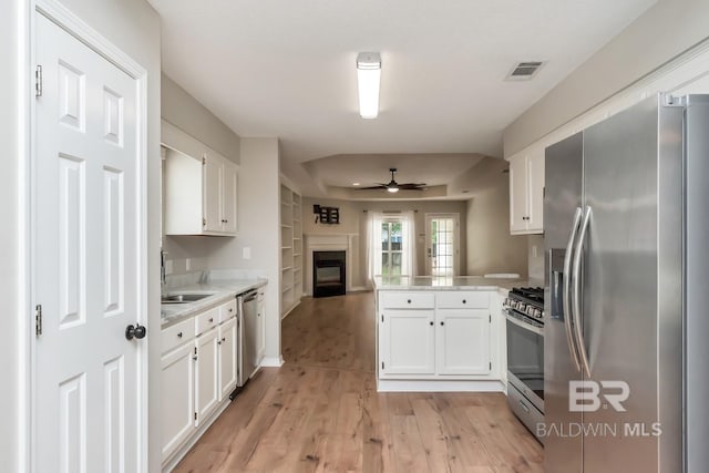 kitchen featuring kitchen peninsula, appliances with stainless steel finishes, light wood-type flooring, ceiling fan, and white cabinetry