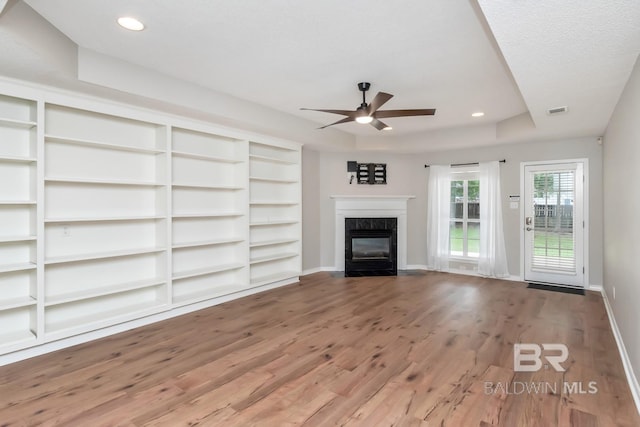 unfurnished living room with ceiling fan, a raised ceiling, a textured ceiling, a fireplace, and hardwood / wood-style flooring