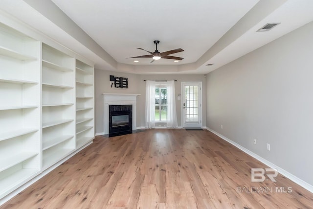 unfurnished living room featuring ceiling fan, light hardwood / wood-style floors, a high end fireplace, and a tray ceiling