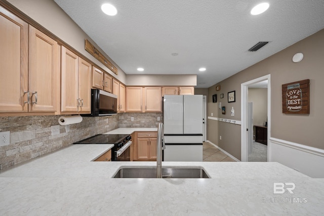 kitchen featuring a sink, range with electric stovetop, freestanding refrigerator, light countertops, and tasteful backsplash