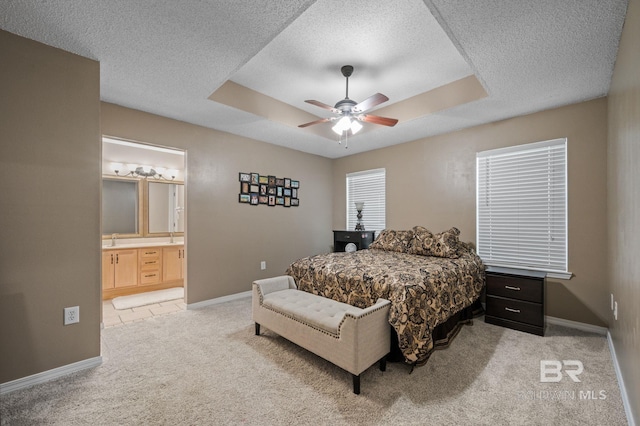 bedroom featuring light colored carpet, a textured ceiling, a tray ceiling, baseboards, and connected bathroom