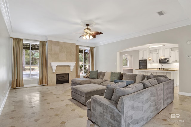 living room with ceiling fan, a fireplace, crown molding, and sink