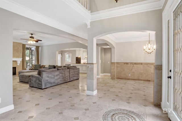 living room featuring tile walls, crown molding, a fireplace, and ceiling fan with notable chandelier