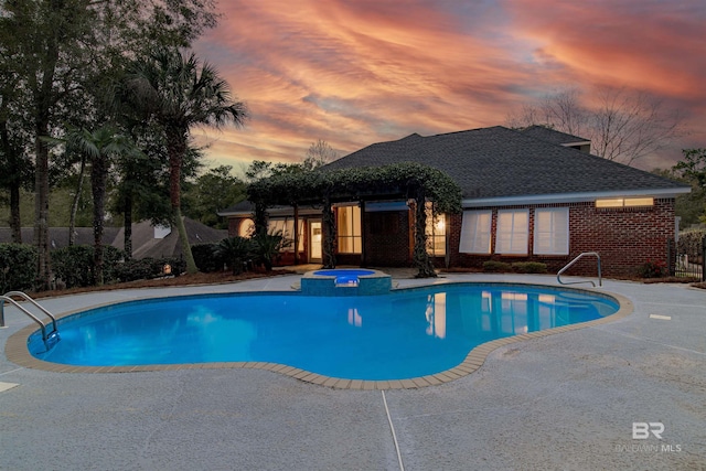 pool at dusk featuring an in ground hot tub and a patio