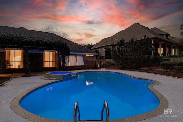 pool at dusk with an in ground hot tub and a patio area