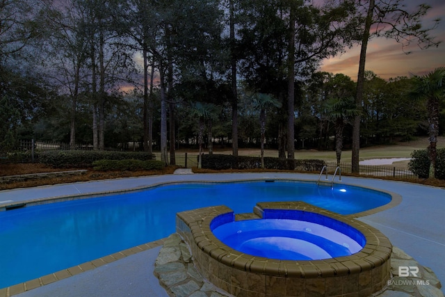 pool at dusk with an in ground hot tub