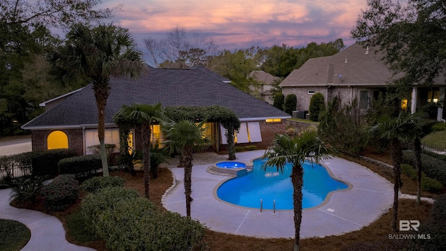 pool at dusk featuring a patio area and an in ground hot tub