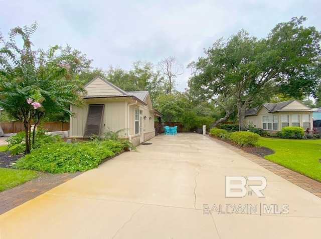 view of side of property with driveway, fence, board and batten siding, and a yard