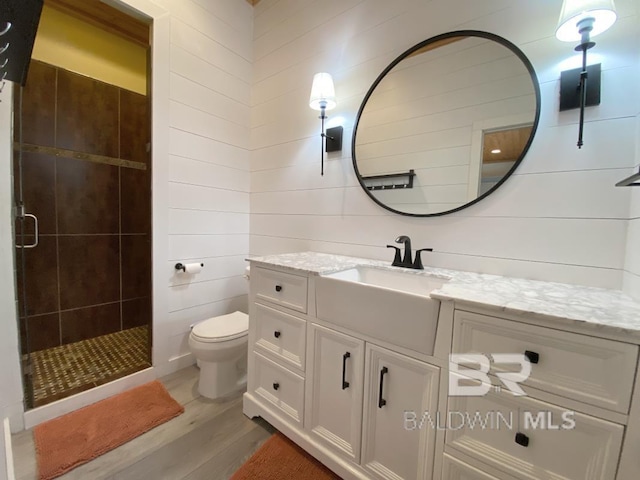 full bath featuring toilet, vanity, a tile shower, and wood finished floors