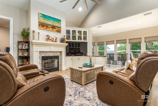 living room with a tiled fireplace, ceiling fan, high vaulted ceiling, and light hardwood / wood-style flooring