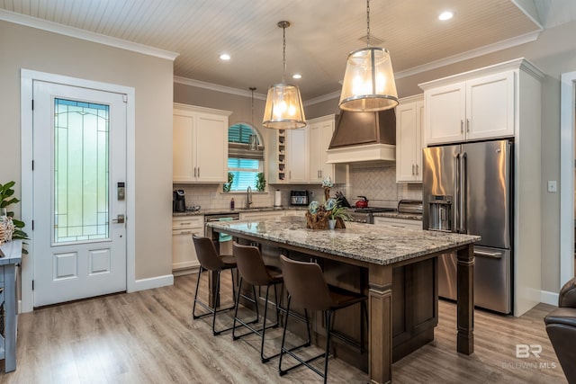 kitchen featuring pendant lighting, stainless steel appliances, custom range hood, white cabinets, and a kitchen island