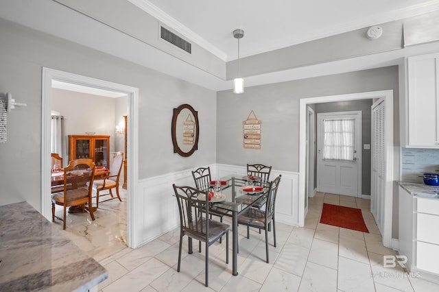 dining space with visible vents, crown molding, marble finish floor, wainscoting, and a decorative wall