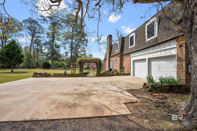 view of property exterior featuring roof with shingles, brick siding, concrete driveway, a lawn, and mansard roof
